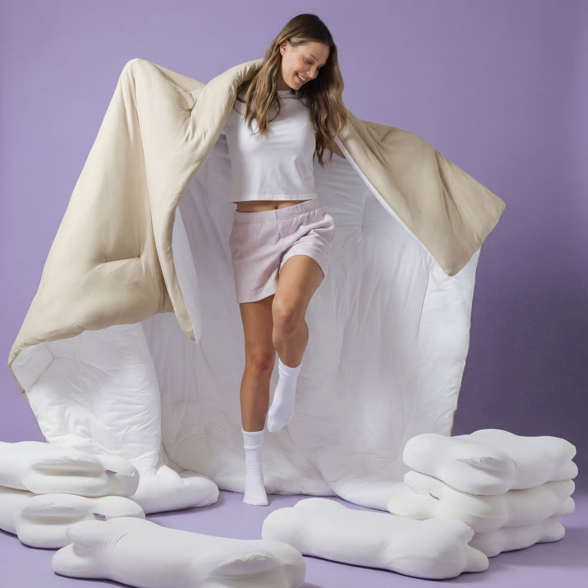 Woman standing with a large white comforter and pillows on a purple background